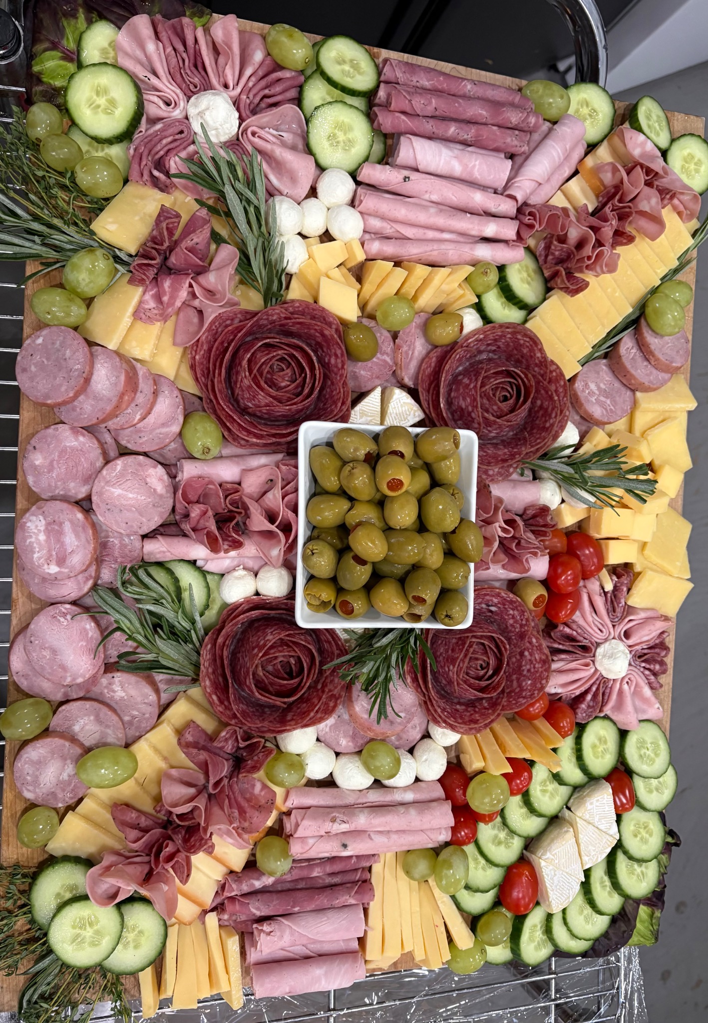 Charcuterie board with assorted meats, cheeses, grapes, cucumber and olives